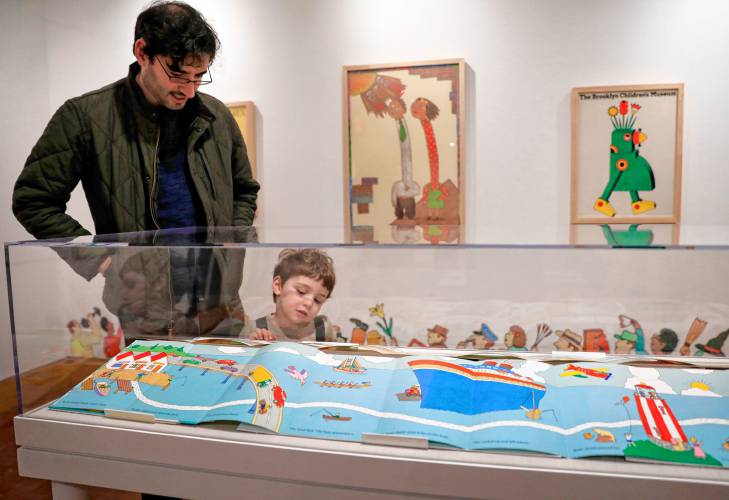 Adam Horowitz and his son Ben, 3, view a fold-out picture book display in the exhibit “Kid in a Candy Store,” featuring work by Seymour Chwast, at the Eric Carle Museum.