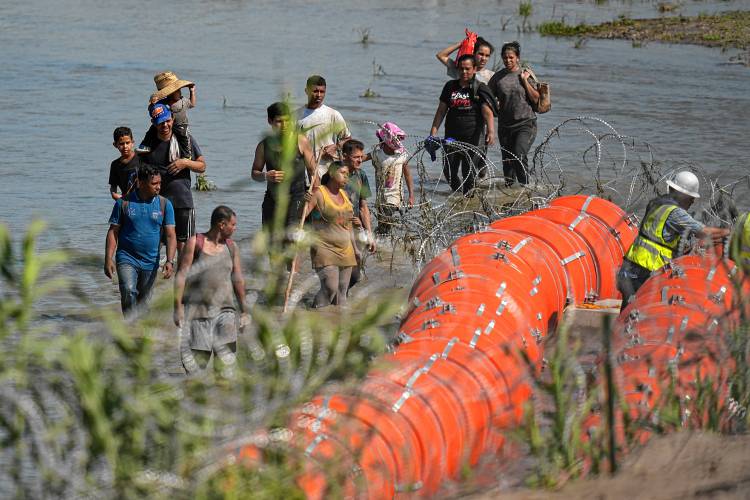 Migrants trying to enter the U.S. from Mexico approach the site where workers are assembling large buoys to be used as a border barrier along the banks of the Rio Grande near Eagle Pass, Texas, last July.